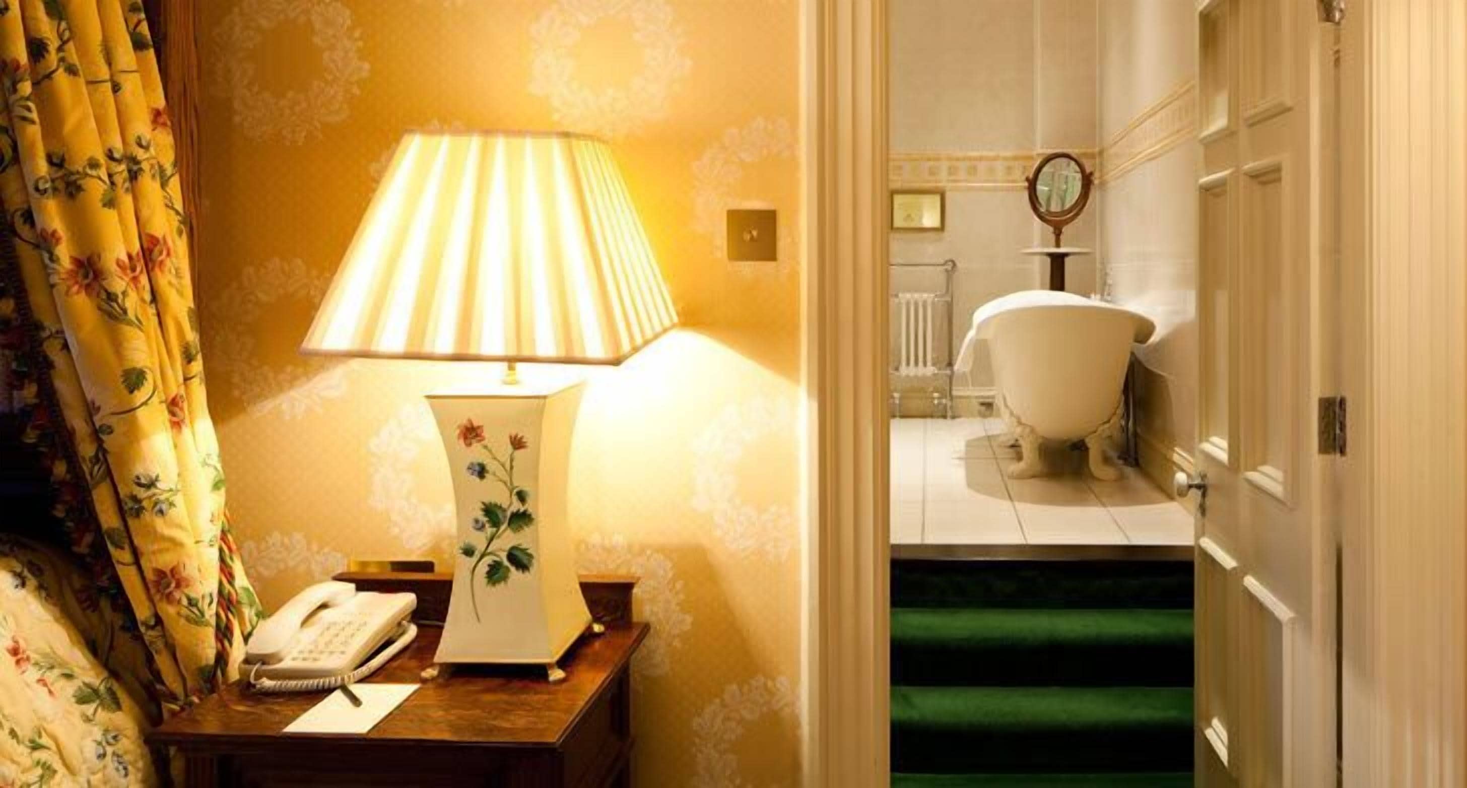 A hotel room with a bedside lamp, a telephone, and a floral-patterned curtain.