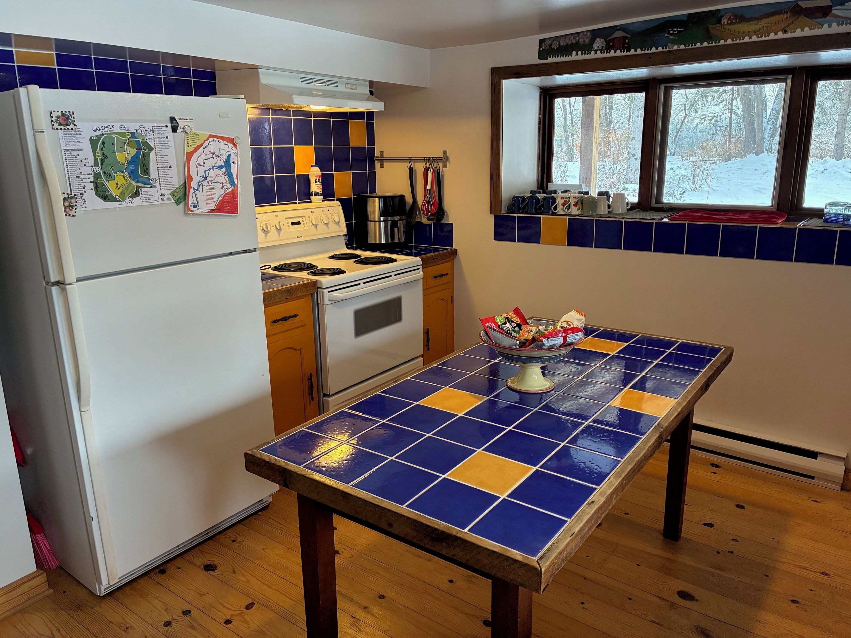 Una cocina con refrigerador, estufa, horno y una mesa con un diseño de azulejos azules y amarillos.