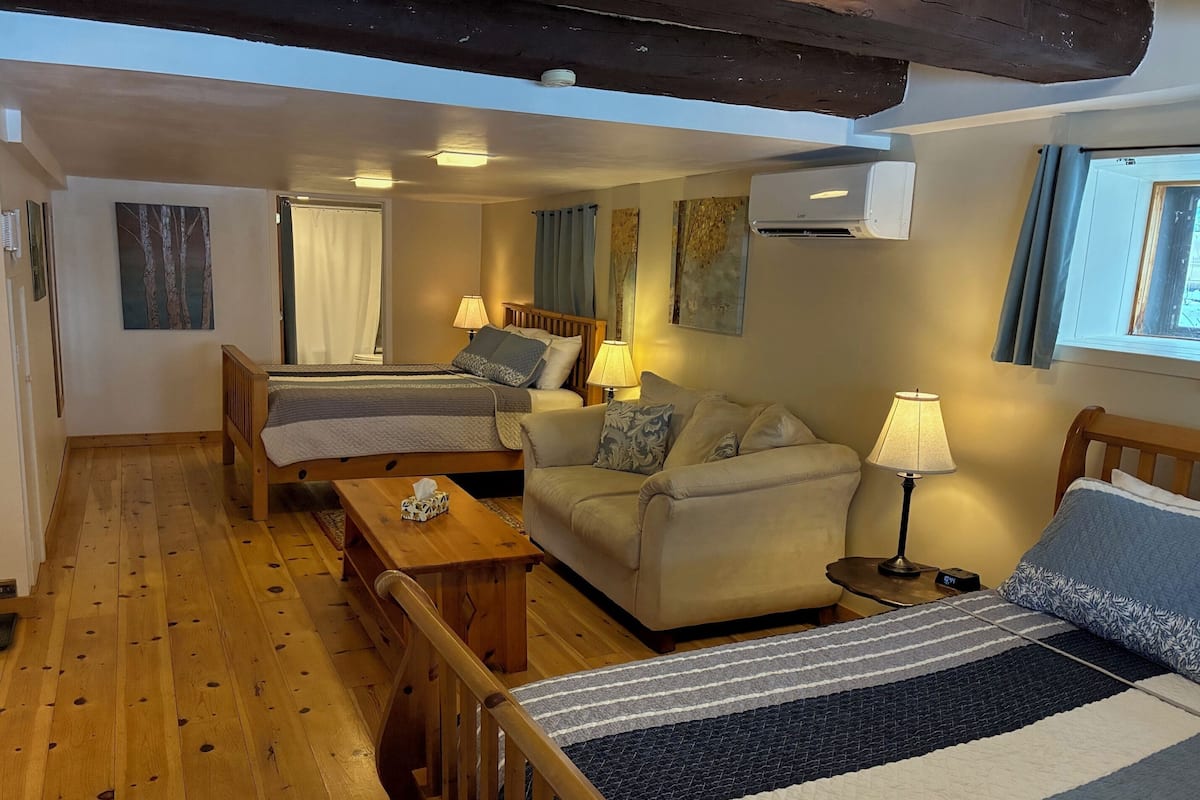 A cozy room with two beds, a sofa, a wooden table, and a lamp.