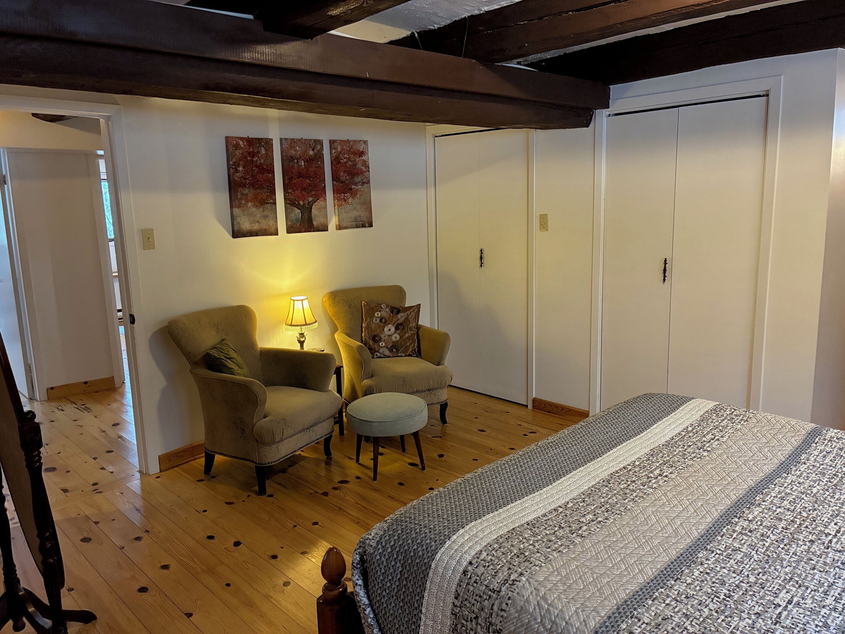Un dormitorio con una cama, dos sillones, una mesita de noche con lámpara y un armario.