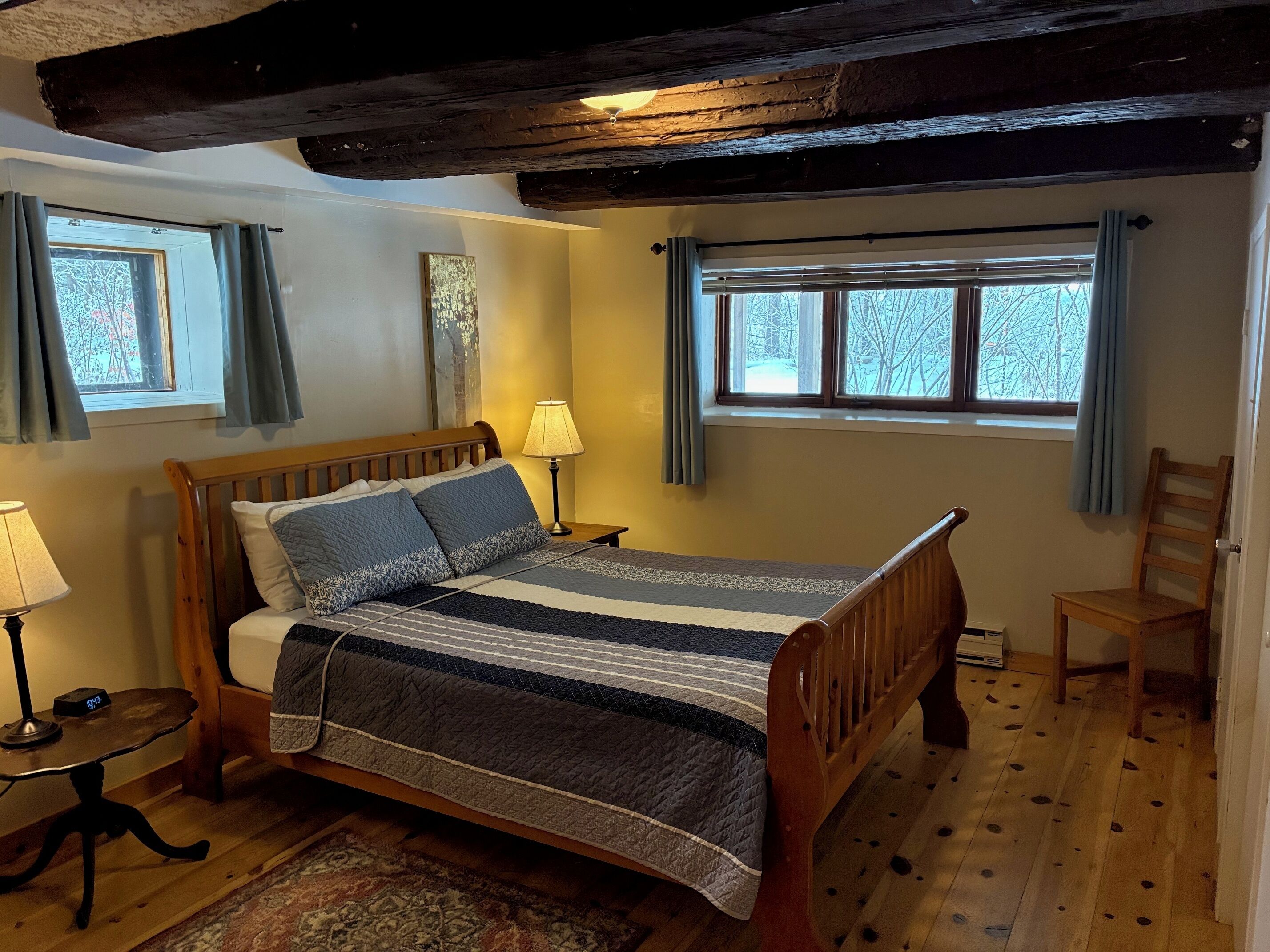 Un dormitorio acogedor con una cama de madera, una mesita de noche con lámpara, una ventana con cortinas y una silla.