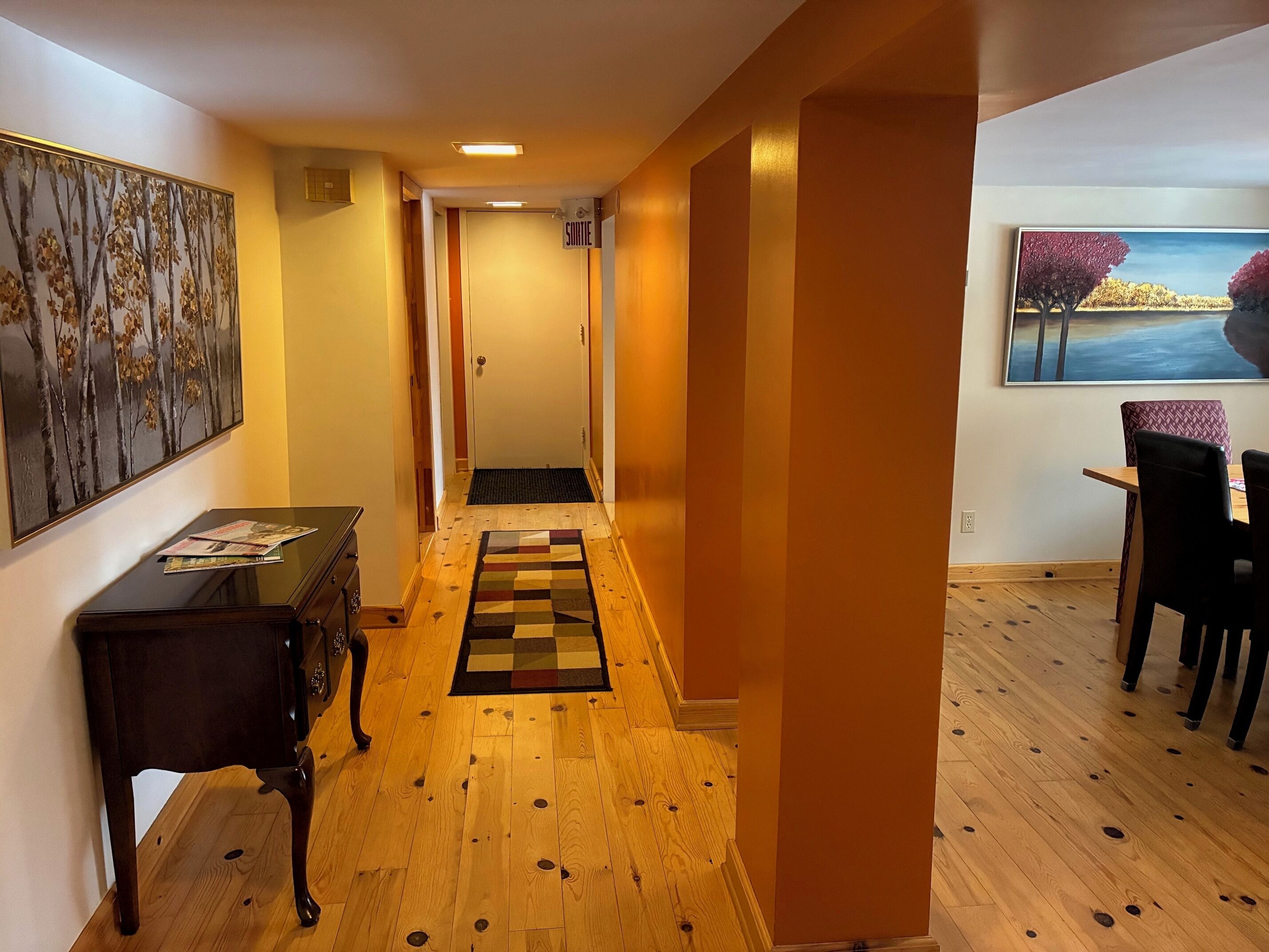 A hallway with wooden flooring, a black console table, a door with a 'SILENT' sign, a patterned rug, and a dining area with a table and chairs.