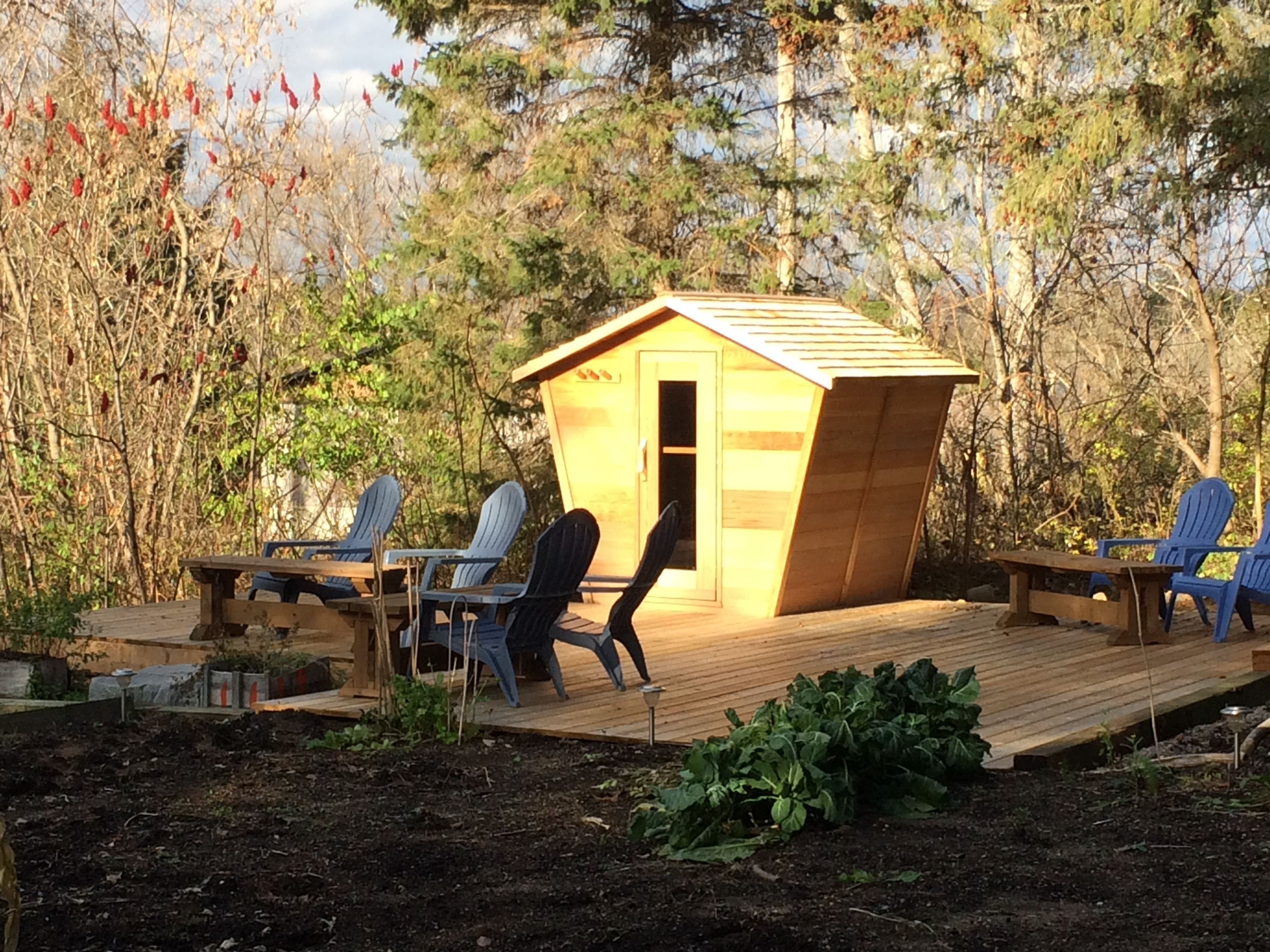 A wooden deck with a small shed, two Adirondack chairs, and a table.