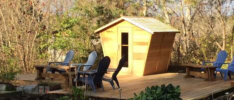 A wooden deck with a small shed, two Adirondack chairs, and a table.