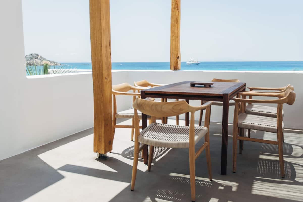A wooden table and chairs on a balcony with a view of the sea and a ship in the distance.