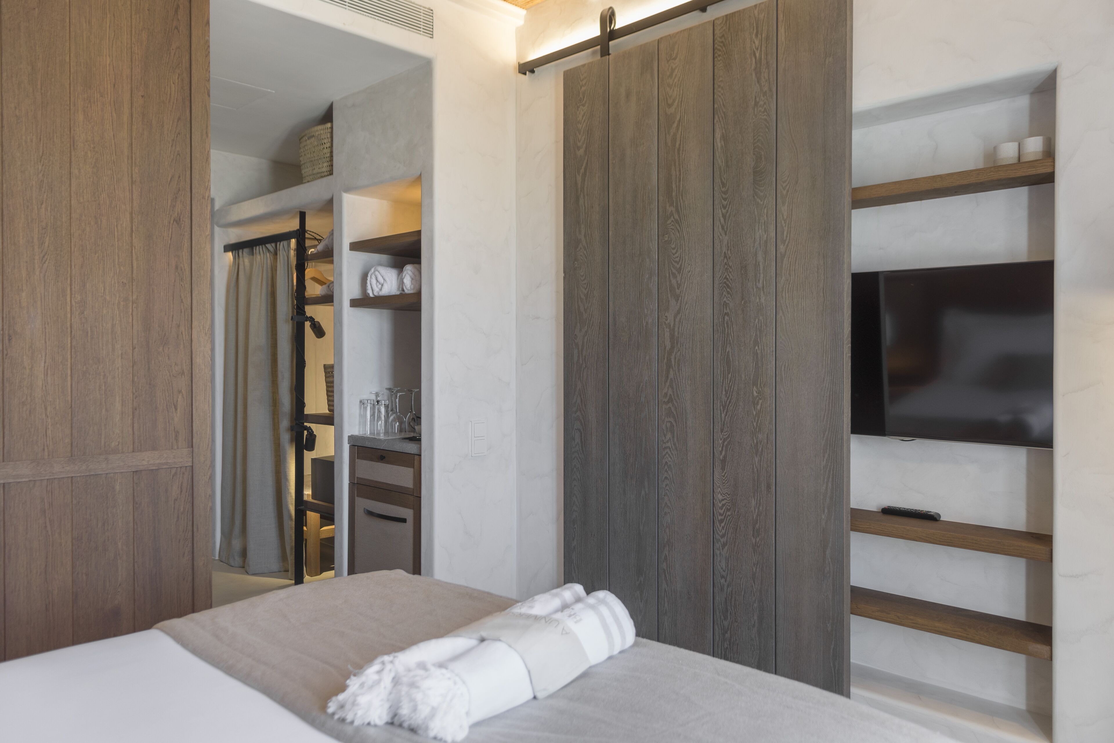 Una habitación de hotel moderna con una cama, televisión, armario y vestidor.
