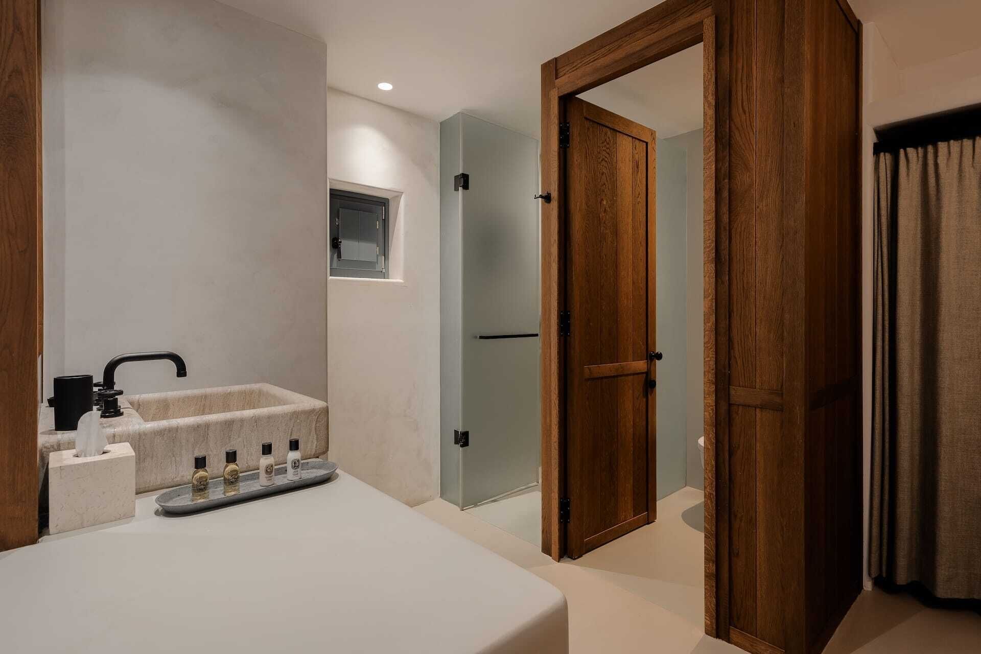 Un baño moderno con un lavamanos blanco, un grifo negro y una encimera de mármol. Se ve una puerta de madera y una ventana con vistas a un pasillo.