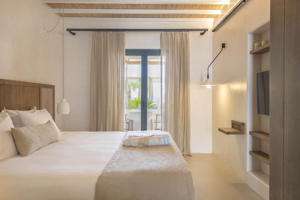A modern hotel room with a large bed, a TV, a desk, and a window with curtains.