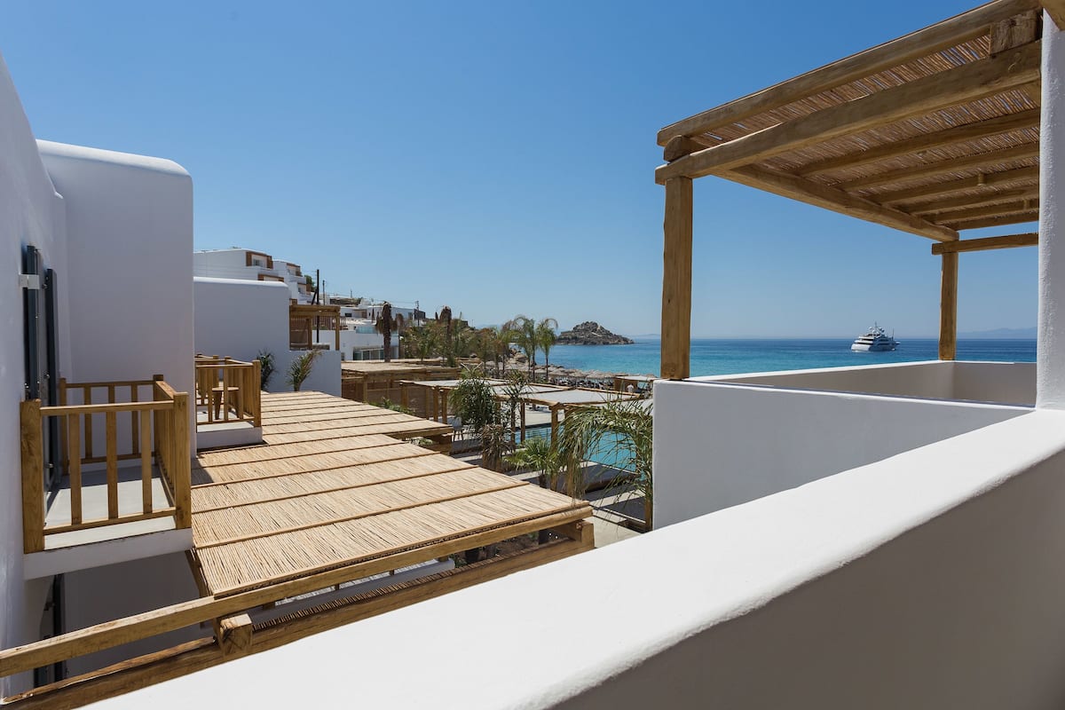 A balcony with wooden flooring, white walls, and a view of the sea and a yacht.