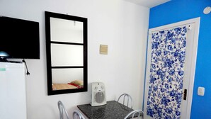 Una habitación pequeña con una mesa, dos sillas, un espejo, un ventilador y una puerta con papel tapiz floral.