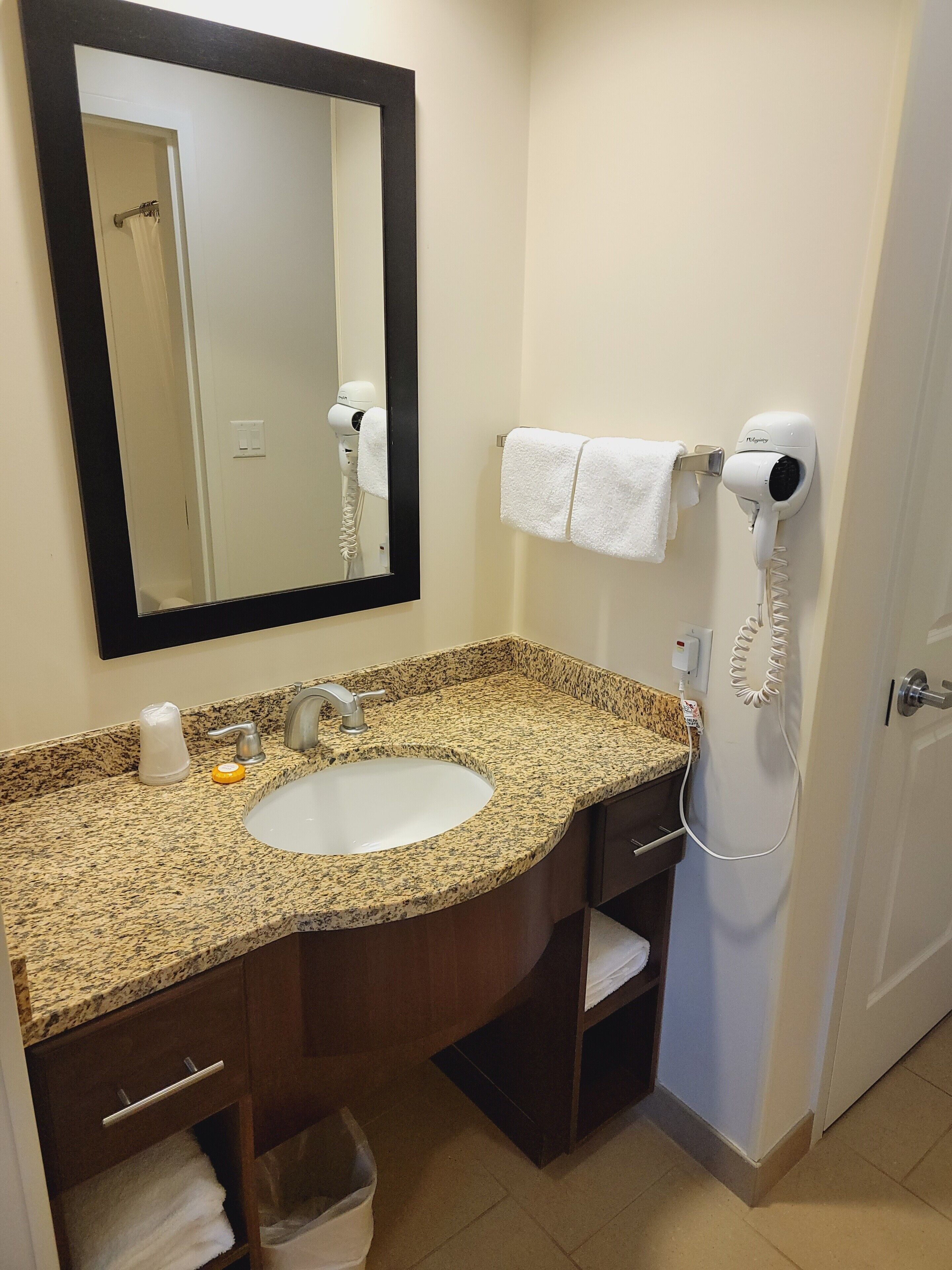 A bathroom with a granite countertop sink, a mirror, a hairdryer, and a towel rack.