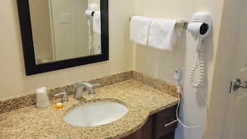 A bathroom with a granite countertop sink, a mirror, a hairdryer, and a towel rack.