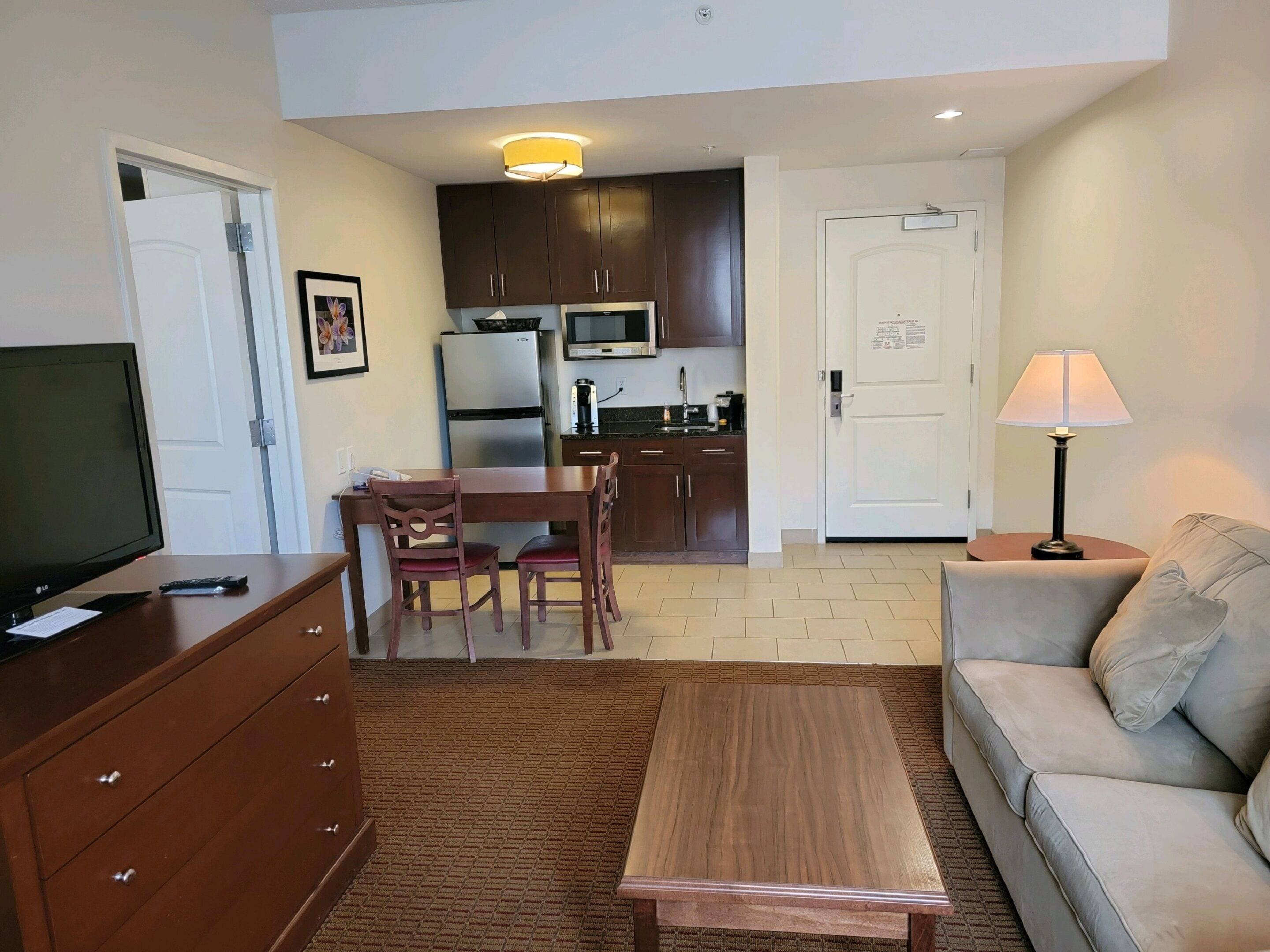 A compact living space with a kitchenette, a dining area, a sofa, a TV, and a lamp.