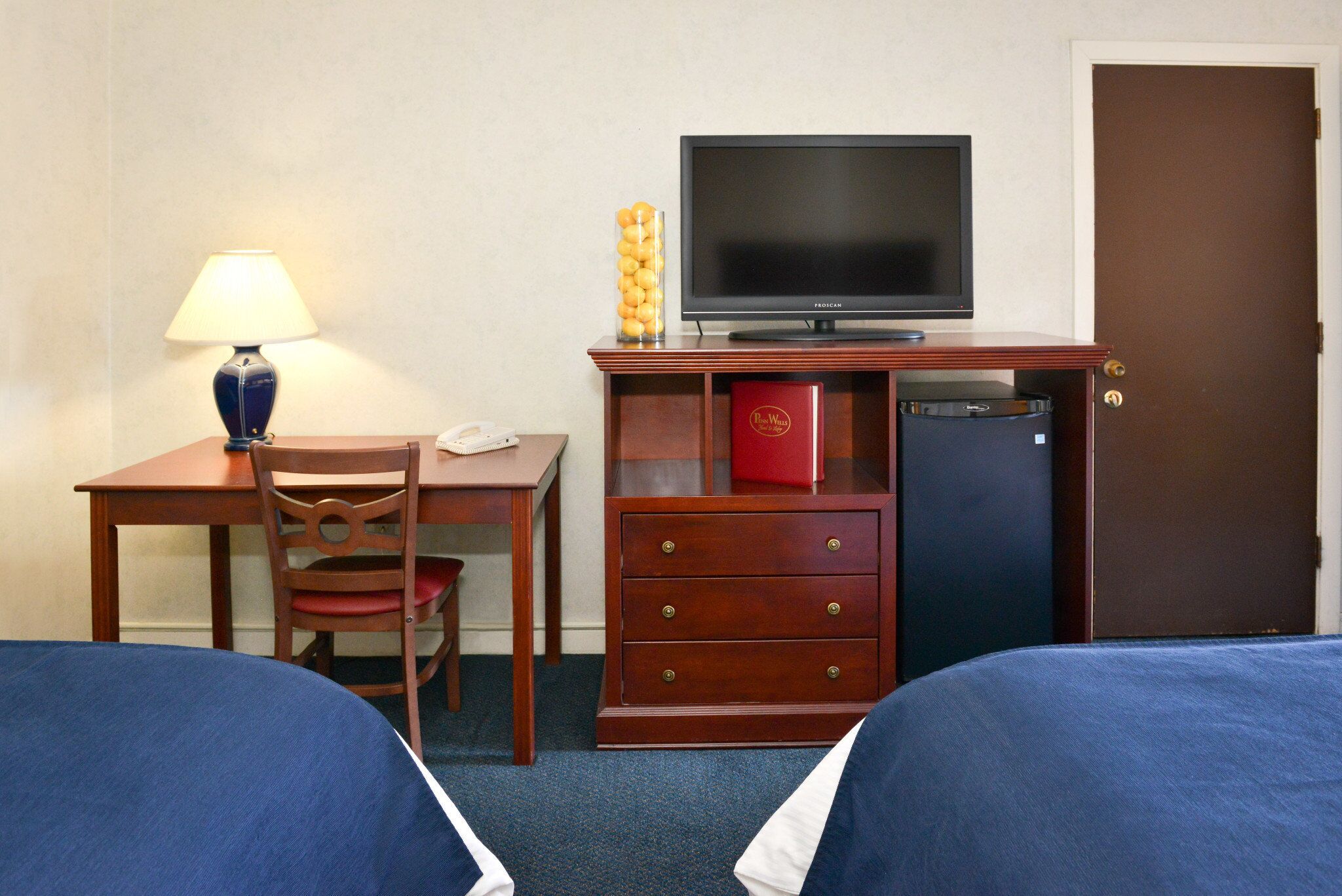 A hotel room with two beds, a desk with a lamp, a television, and a minibar.
