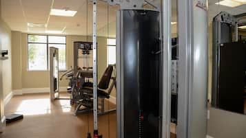Uma academia com equipamentos de exercícios, um banco de musculação e um espelho grande.