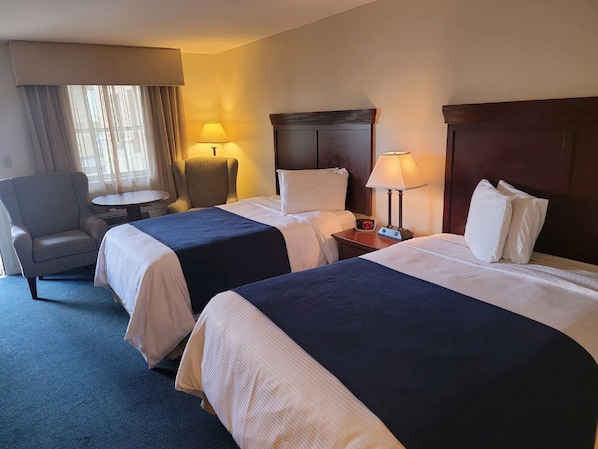 Habitación de hotel con dos camas, una silla, una mesita y dos lámparas.