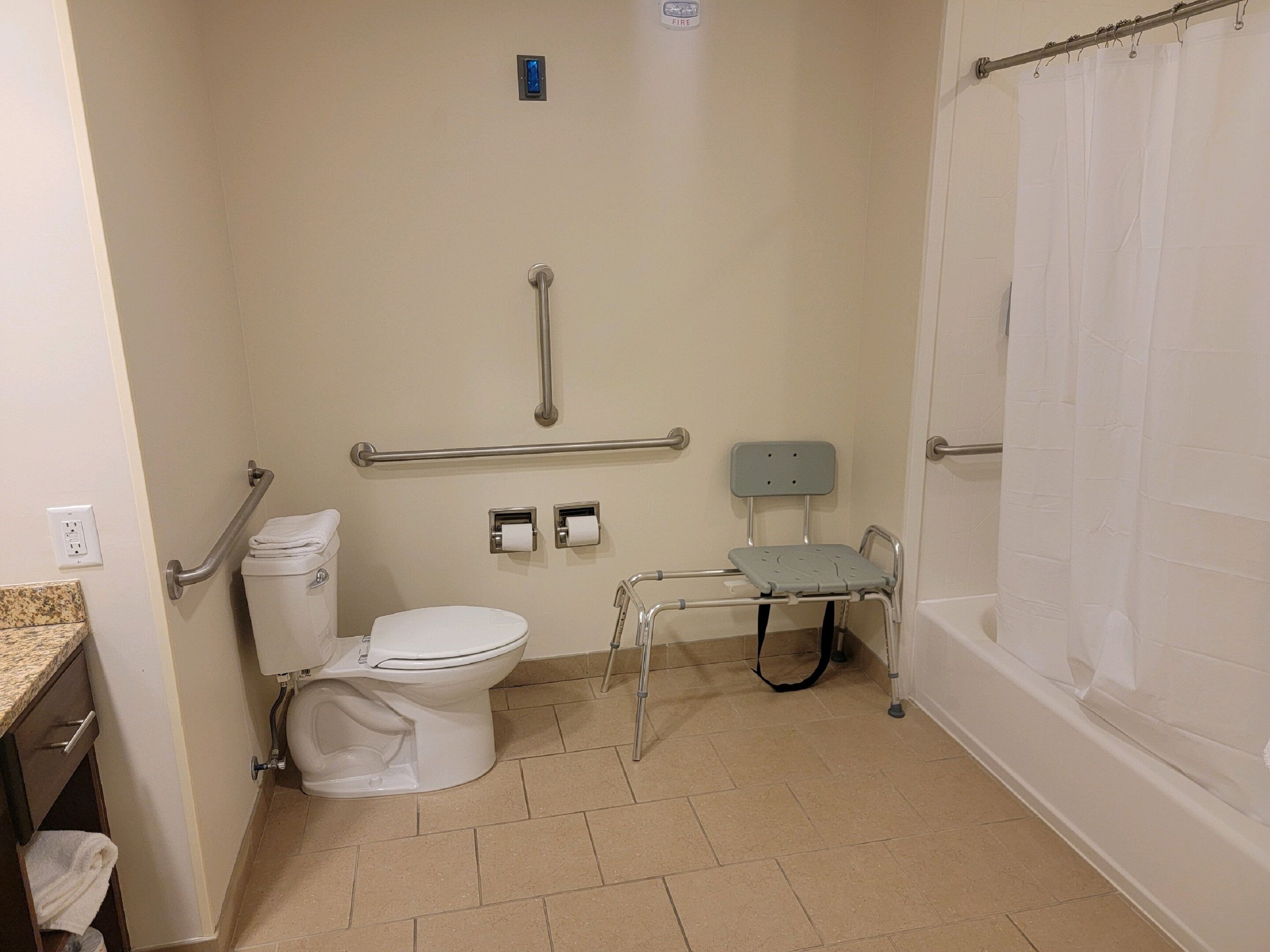 A bathroom with a toilet, a grab bar, a shower chair, and a bathtub.