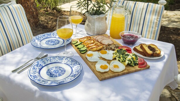 A table set outdoors with a variety of breakfast items including eggs, tomatoes, cucumbers, and bread. - Meleni Cottage Houses (Pareklisia)