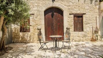 A stone building with a large wooden door, two metal tables with chairs, and a tree.