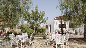 An outdoor patio with stone flooring, white furniture, and a view of a white building with wooden shutters.