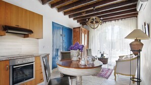 A kitchen with wooden cabinets, a built-in oven, a dining table with a vase of purple flowers, and a chandelier. - Meleni Cottage Houses (Pareklisia)
