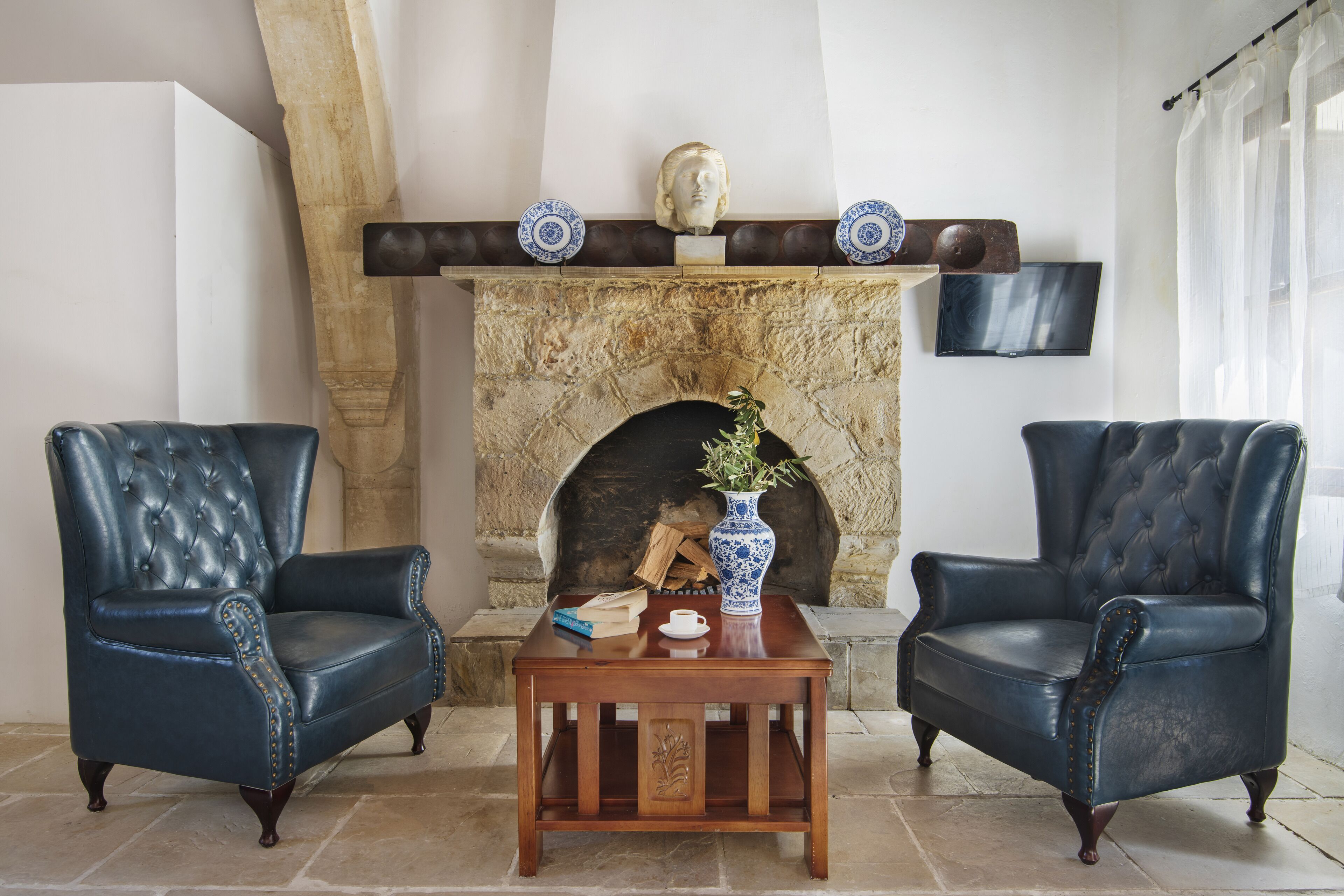 Una habitación con dos sillones de cuero, una mesa de centro de madera, una chimenea de piedra y un televisor fijado a la pared.