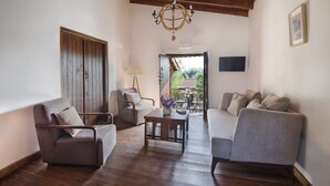 A cozy living room with a wooden ceiling, a chandelier, and a view of the outdoors through an open door. - Meleni Cottage Houses (Pareklisia)