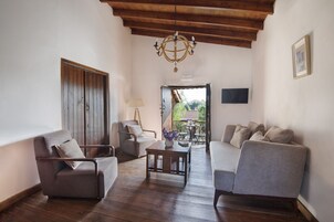 Una sala de estar acogedora con techo de madera, un candelabro y vistas al exterior a través de un ventanal abierto.