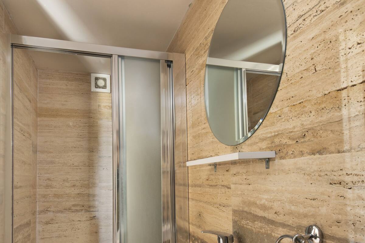 A bathroom with a glass-enclosed shower, a white sink, and a wall-mounted mirror.