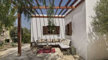A covered outdoor seating area with a white wall, wooden furniture, and a pergola.