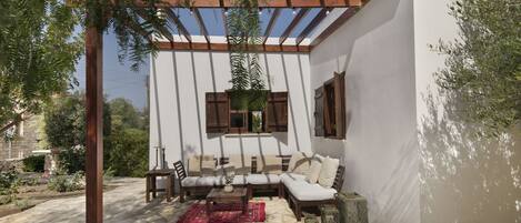 A covered outdoor seating area with a white wall, wooden furniture, and a pergola.