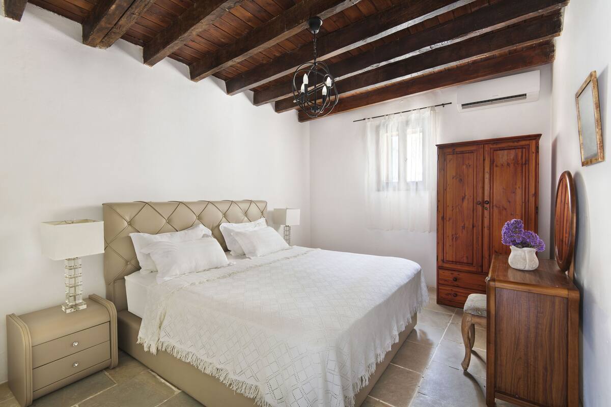 A bedroom with a bed, nightstand, dresser, and a wooden ceiling.