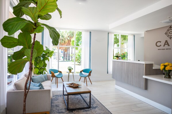 A modern hotel lobby with a sofa, two chairs, a coffee table, and a reception desk. - Casa Boutique Hotel (Miami Beach)