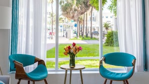 Two teal chairs with wooden legs and a small round table with a vase of flowers between them. - Casa Boutique Hotel (Miami Beach)