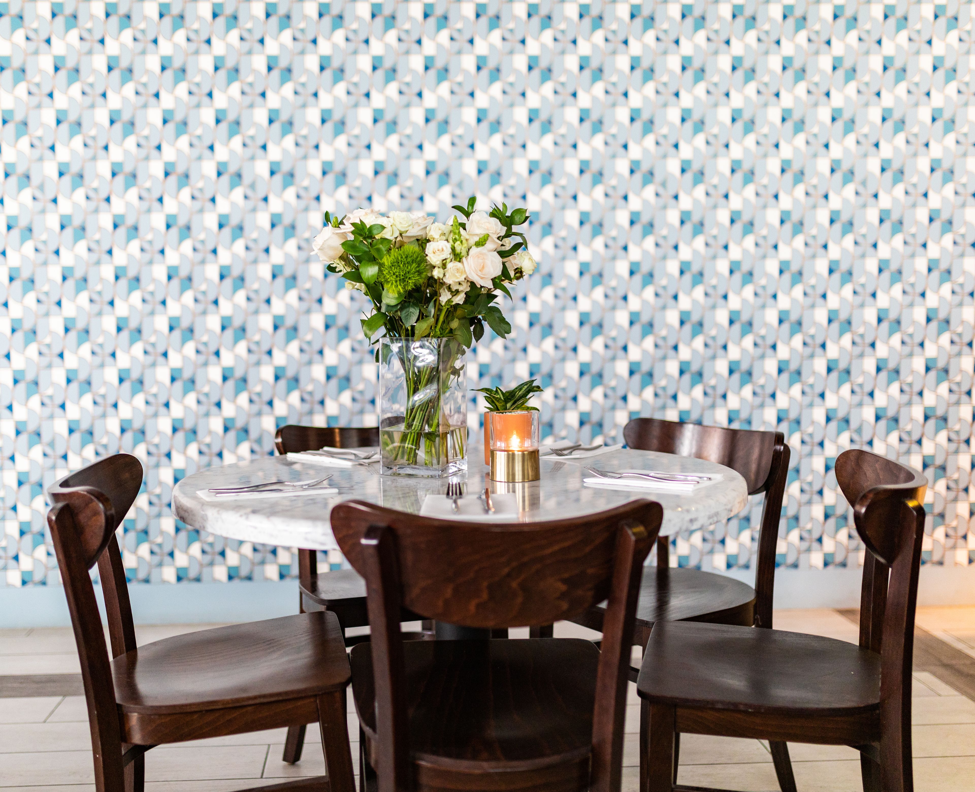 A round dining table with four chairs, a vase with flowers, and a candle on the table.