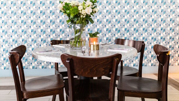 A round dining table with four chairs, a vase with flowers, and a candle on the table. - Casa Boutique Hotel (Miami Beach)