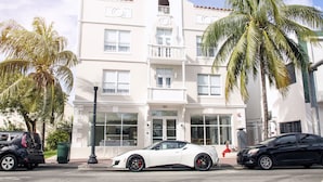 A white building with a balcony, palm trees, and parked cars. - Casa Boutique Hotel (Miami Beach)