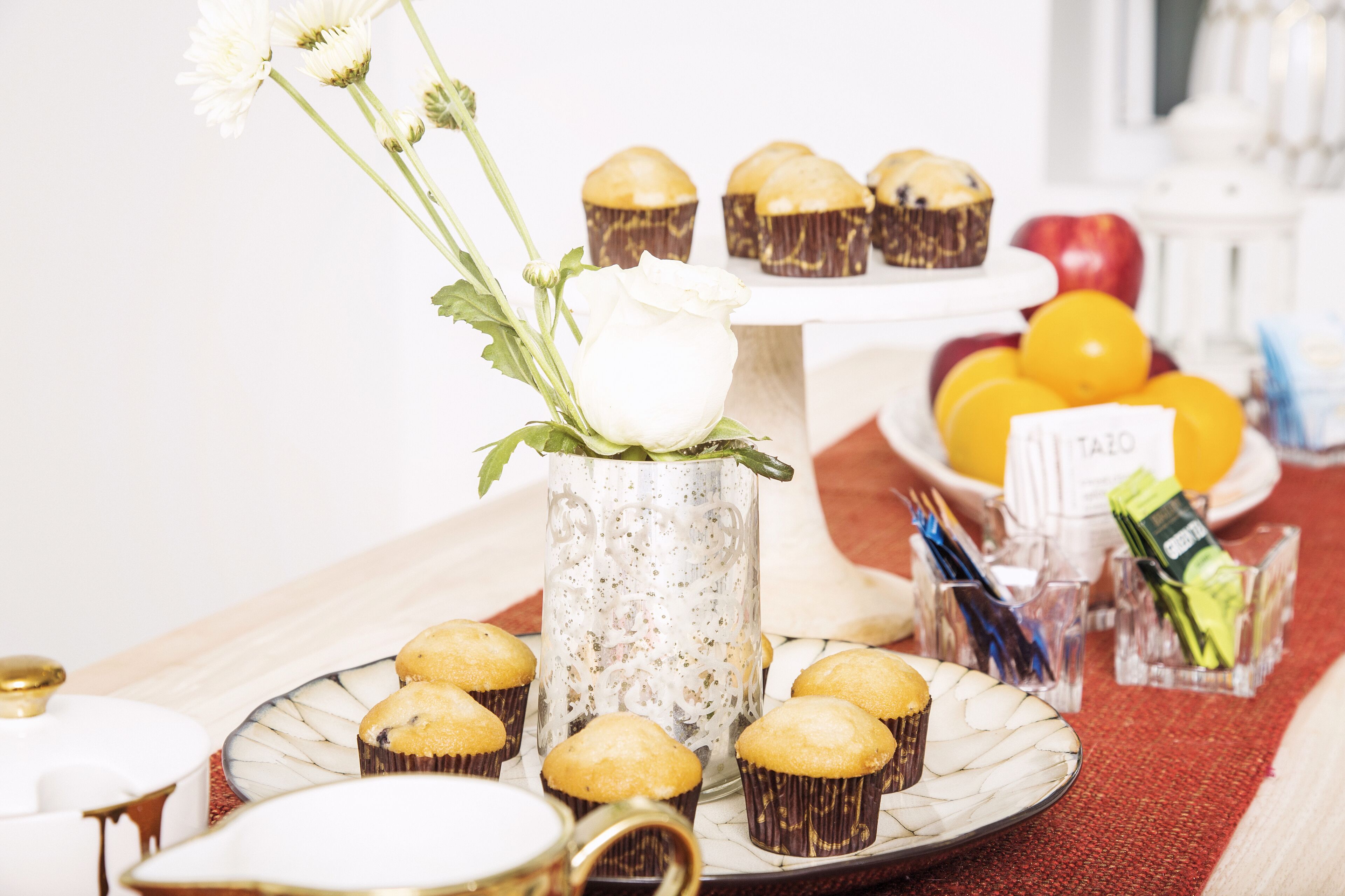 Une table avec des cupcakes, un vase contenant une fleur blanche et un saladier rempli de fruits.