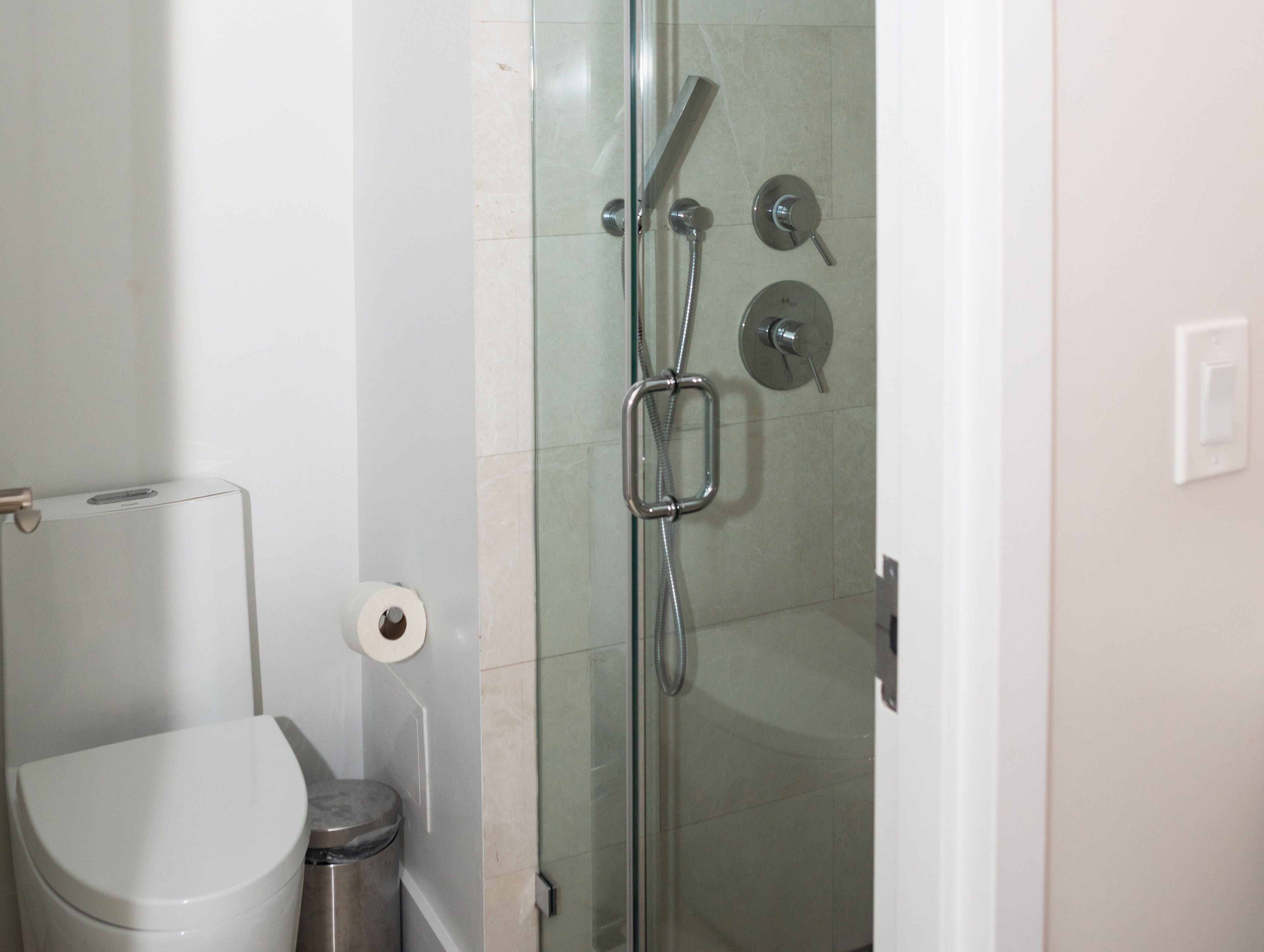 A bathroom with a toilet, a glass-enclosed shower, and a trash can.