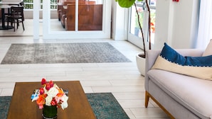 A modern living room with a sofa, a coffee table with flowers, a potted plant, and a view of the dining area through glass doors. - Casa Boutique Hotel (Miami Beach)