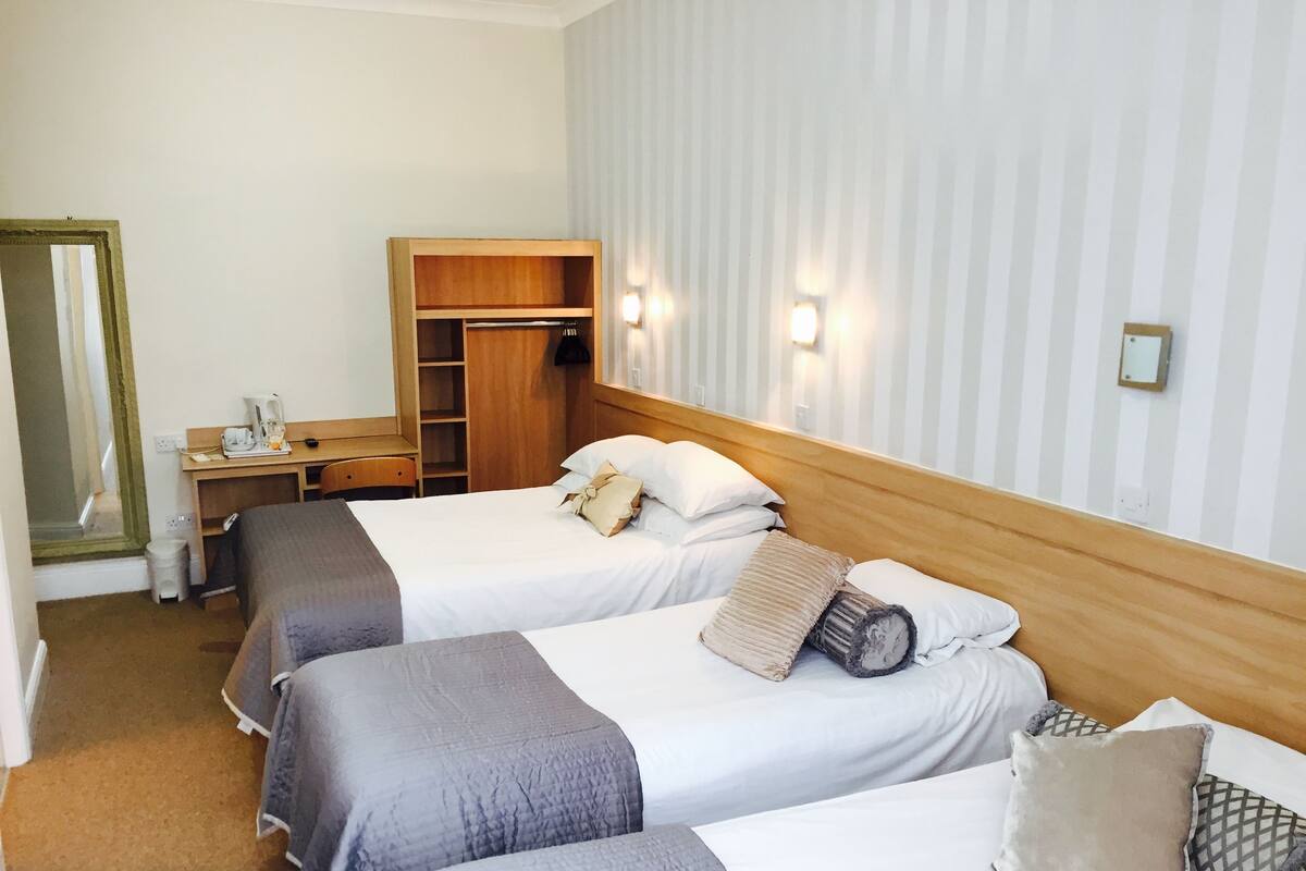 A hotel room with two beds, a wooden wardrobe, a desk with a chair, and a mirror.