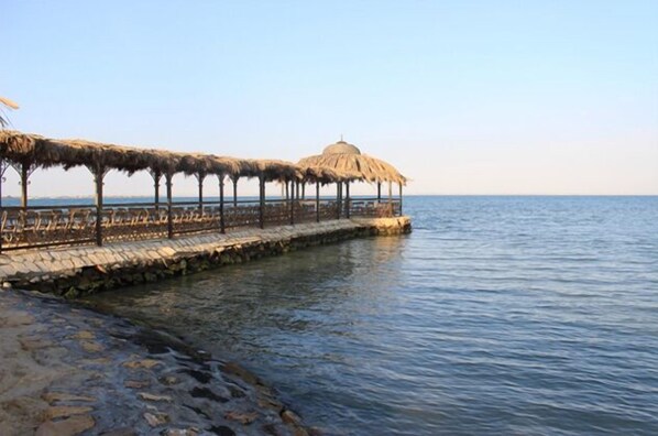 A seaside walkway with thatched umbrellas and a stone railing.