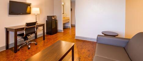 A modern living room with a sofa, a wooden coffee table, a desk with a chair, a flat-screen TV, and a refrigerator.
