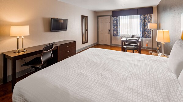 Ein Hotelzimmer mit Bett, Schreibtisch, Stuhl, Fernseher und einer Essecke mit Stühlen und Tisch.