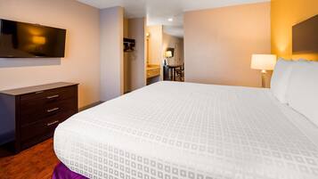 Quarto de hotel com uma cama grande, cômoda, televisão fixada na parede e banheiro visível através de uma porta aberta.