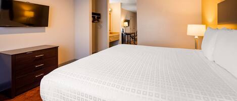 Hotellihuone, jossa on suuri sänky, lipasto, seinälle asennettu televisio ja kylpyhuone, joka näkyy avoimesta ovesta.