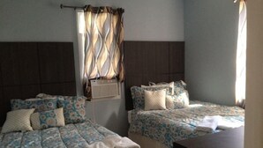 Habitació amb dos llits, cada un amb roba de llit i almoines florals a conjunt. Hi ha una finestra amb cortines, un aparell d'aire condicionat i una taula petita.