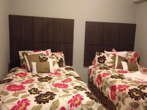 Dos camas individuales con ropa de cama floral, cabeceras oscuras y una pared lisa.