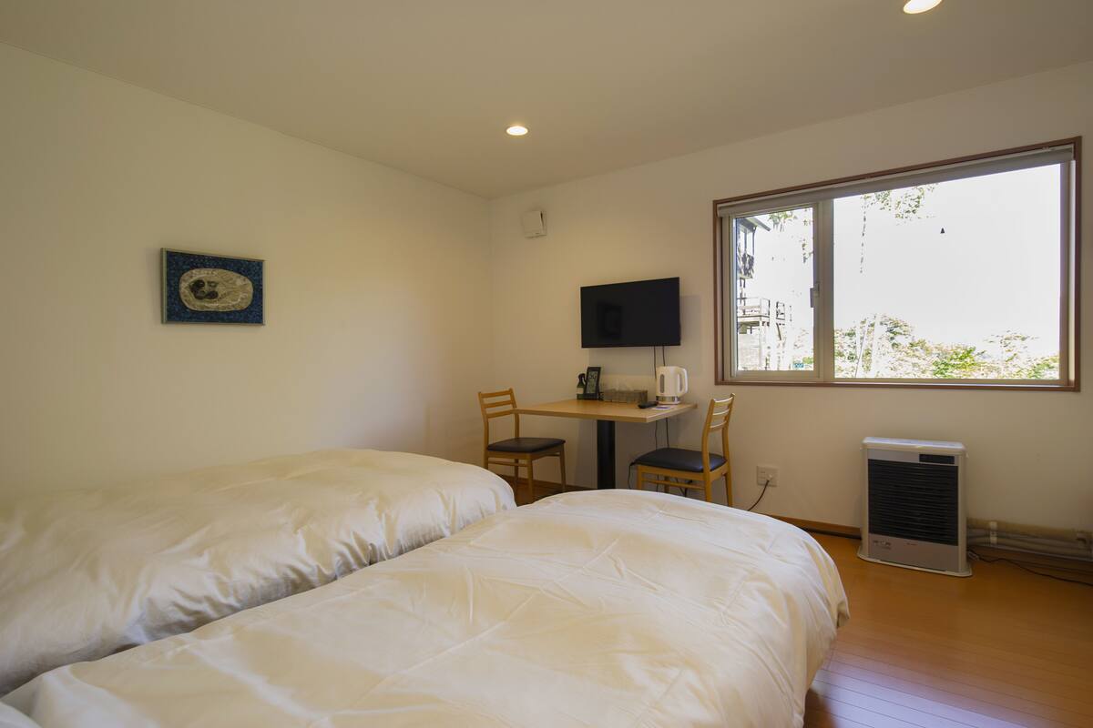 A room with two beds, a desk with a chair, a television, and a window.
