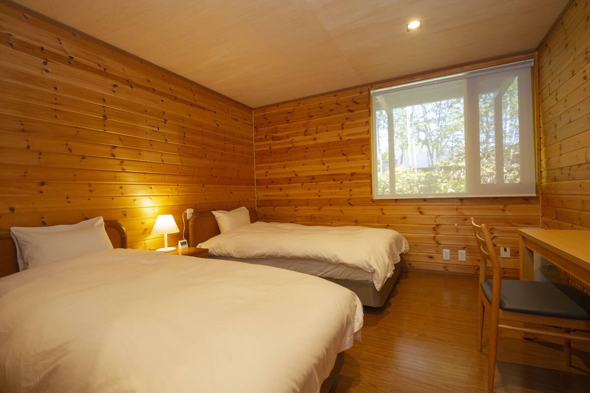 A wooden cabin room with two beds, a table, and a window.